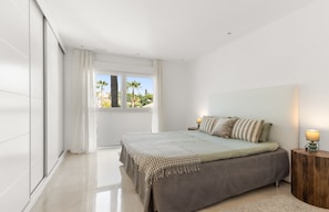 A modern bedroom with a large bed, a view of palm trees, and a balcony.