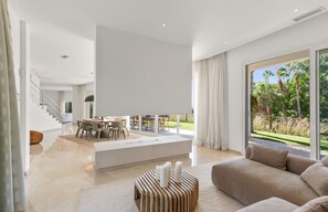 A spacious living area with a large window, a dining area, and a staircase leading to an upper floor.