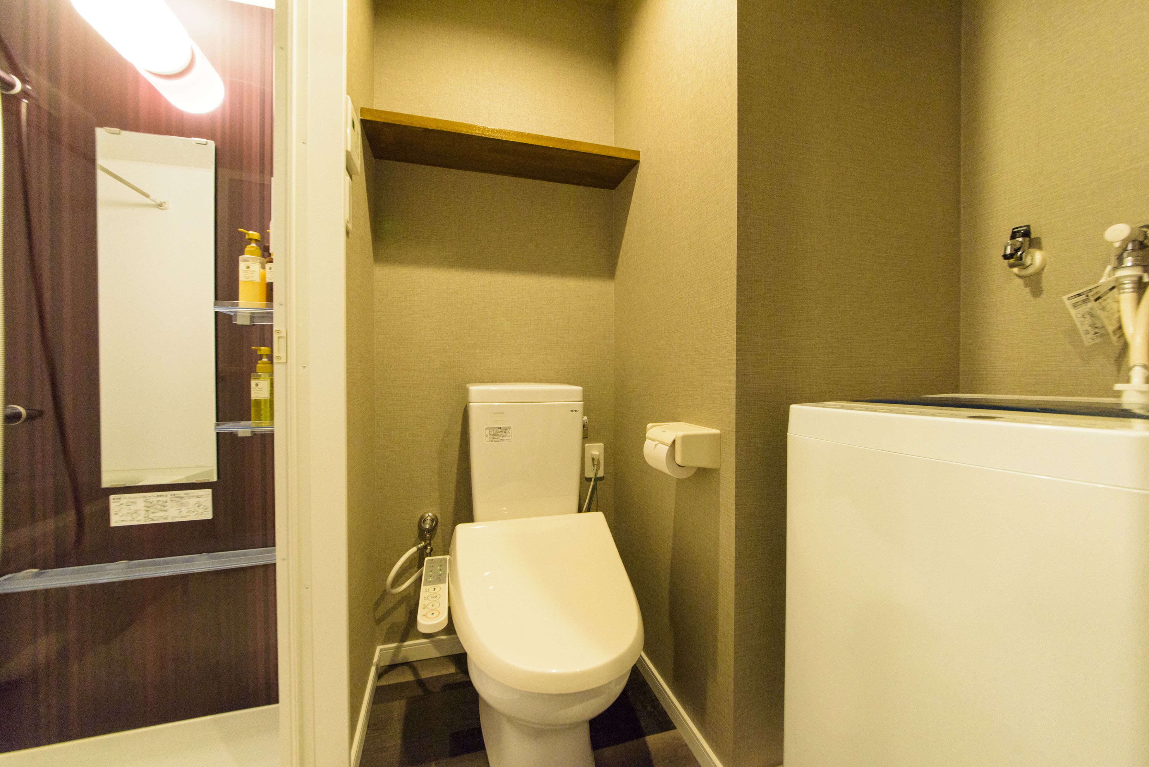 Un baño pequeño con inodoro, un estante sobre el inodoro, dispensador de toallas de papel en la pared y secador de manos.