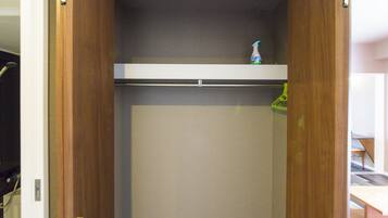 Un dressing accessible sans porte, avec une porte en bois, une étagère sur laquelle se trouve une bouteille et une tringle pour suspendre les vêtements.
