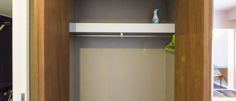 A walk-in closet with a wooden door, a shelf with a bottle, and a hanging rack.