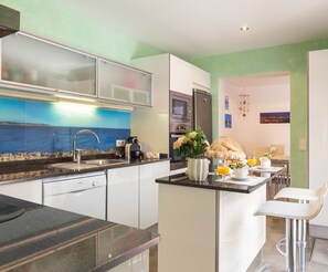 A modern kitchen with a view of the sea, a dining area with a table set for two, and a refrigerator.