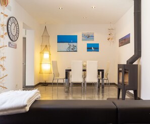 A modern living room with a sofa, clear chairs, a dining table, and artwork on the walls.