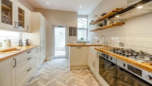 Een moderne keuken met witte kasten, een visgraatvloer, een gasfornuis en houten aanrechtbladen.