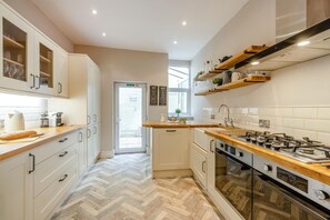 Una cocina moderna con armarios blancos, piso de espiga y encimera de madera, además de una estufa a gas.