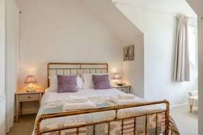 Un dormitorio con una cama, dos mesitas de noche, una lámpara auxiliar, una ventana y una silla.