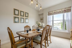 Une salle à manger avec une table en bois, des chaises, des tableaux encadrés au mur et une fenêtre donnant sur un beau paysage.