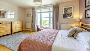 Een slaapkamer met een bed, een dressoir, een stoel, een raam en een lamp.