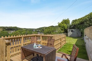 A wooden deck with a table and chairs, a small shed, and a view of a green landscape.