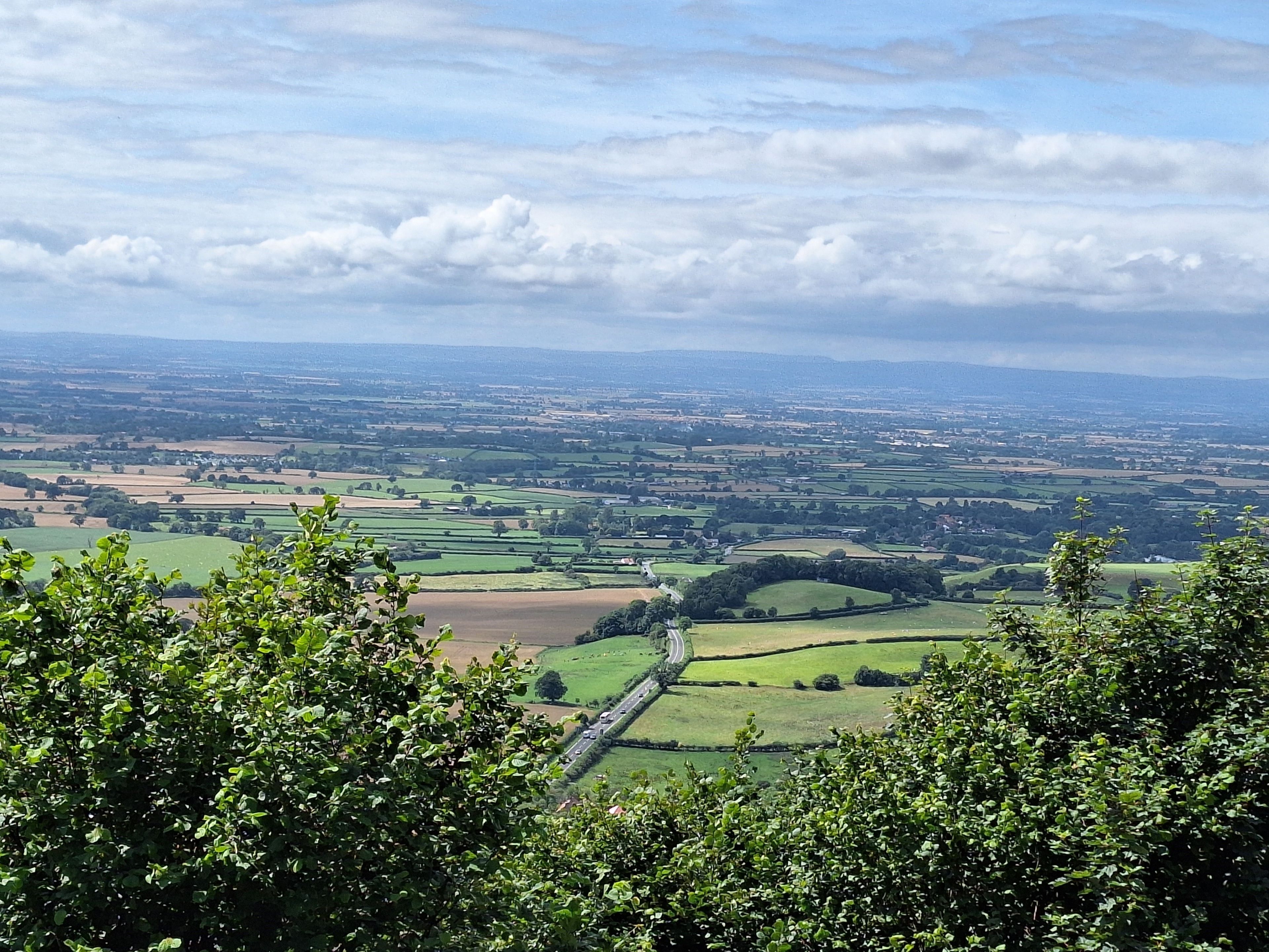 A panoramic view of a rural landscape with fields, a winding road, and distant hills.