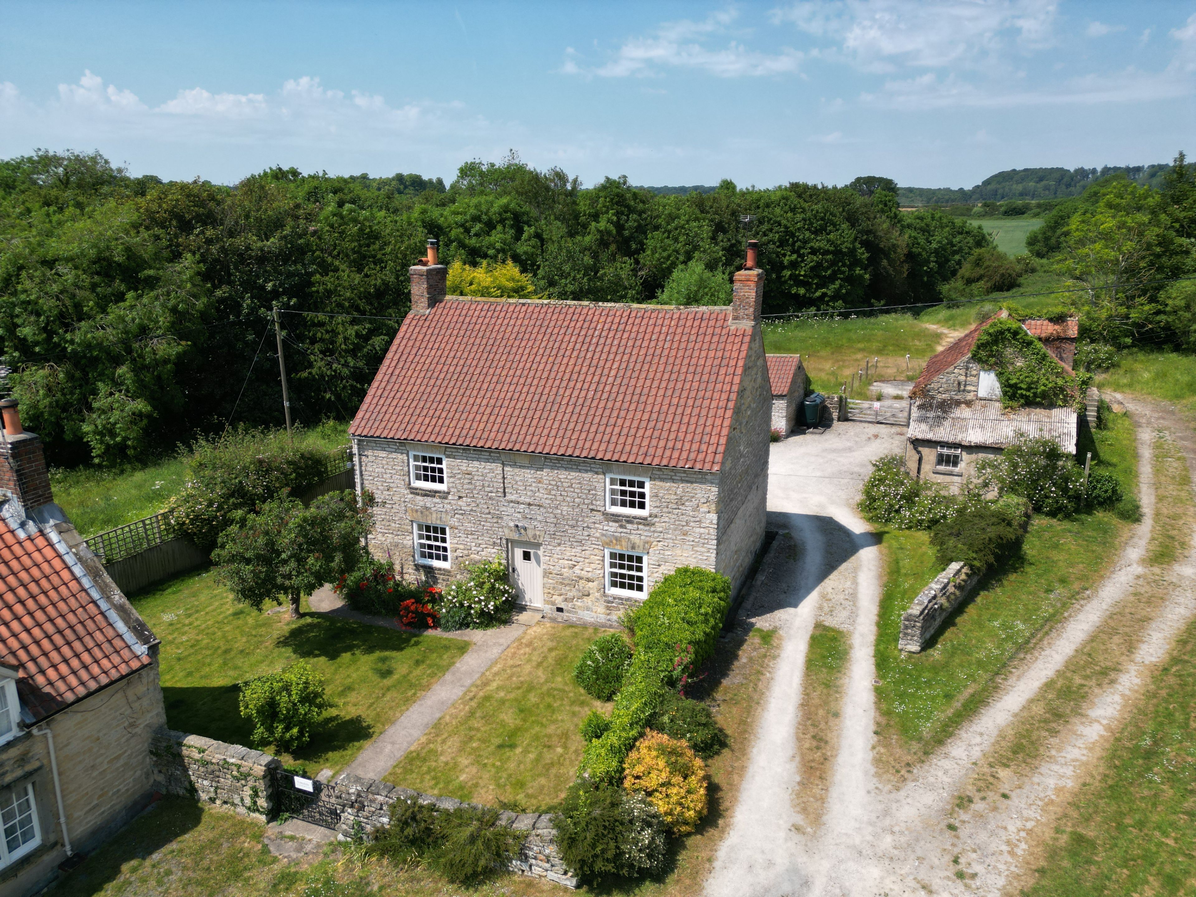 A stone house with a red-tiled roof, surrounded by a well-maintained garden and a gravel driveway.