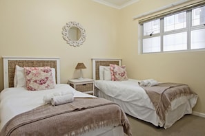 Quarto com duas camas, cada uma com cabeceira, luminária de cabeceira e um espelho na parede.