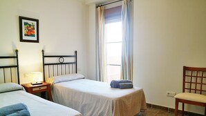 A room with two beds, a chair, a nightstand with a lamp, and a window with curtains. - El Rincon del Golf III - Isla Canela Golf GRHIII99P99 (Isla Canela)