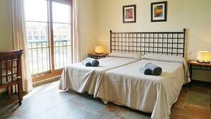 A double room with two beds, a wooden chair, a balcony with a view, and two framed pictures on the wall. - El Rincon del Golf III - Isla Canela Golf GRHIII99P99 (Isla Canela)