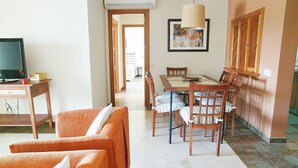 A living room with a TV, orange sofa, dining table with chairs, and a painting on the wall. - El Rincon del Golf III - Isla Canela Golf GRHIII99P99 (Isla Canela)