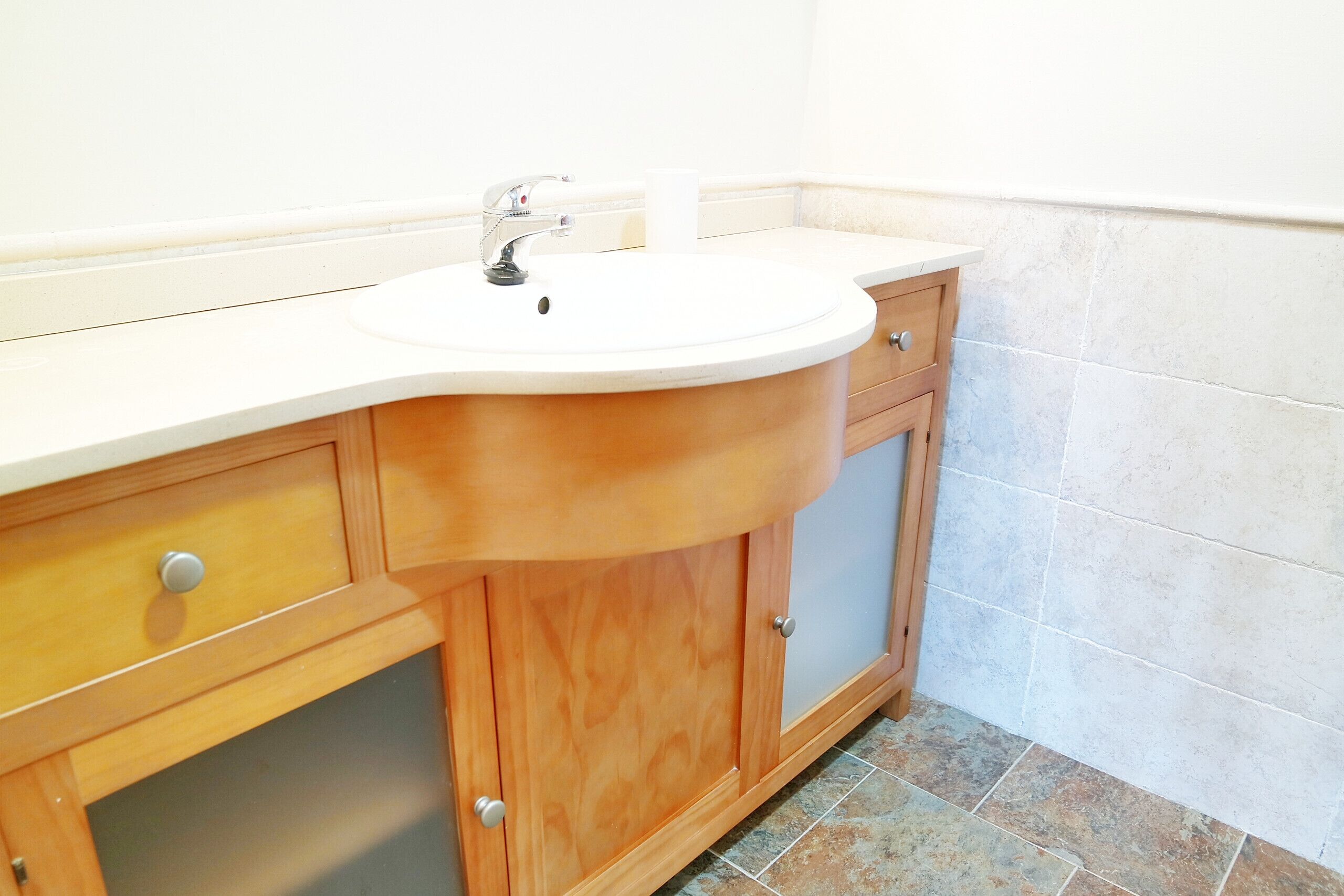 Une salle de bain avec un lavabo blanc, des meubles en bois et un sol carrelé.