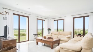 A spacious living room with large windows, a wooden coffee table, a beige sofa, and a television on a wooden cabinet. - CAN SAL - Villa with private pool in and free WiFi in Ariany (Ariany)