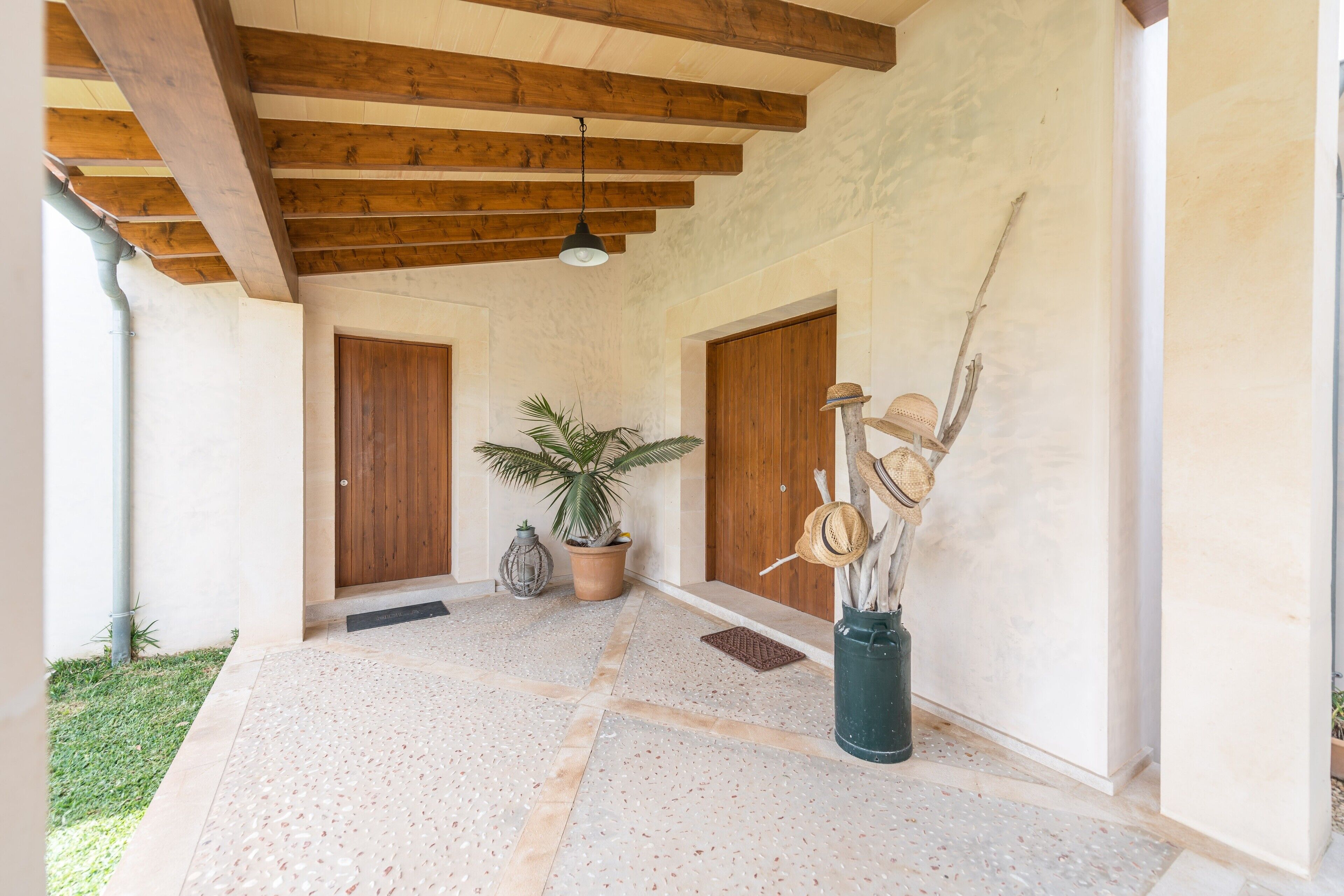A covered outdoor area with a tiled floor, wooden beams, and two wooden doors.