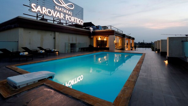 A swimming pool with lounge chairs and a sign for 'Nataraj Sarovar Portico'. - Nataraj Sarovar Portico Jhansi (Jhansi)