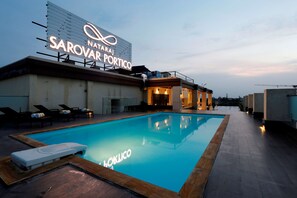 A swimming pool with lounge chairs and a sign for 'Nataraj Sarovar Portico'. - Nataraj Sarovar Portico Jhansi (Jhansi)