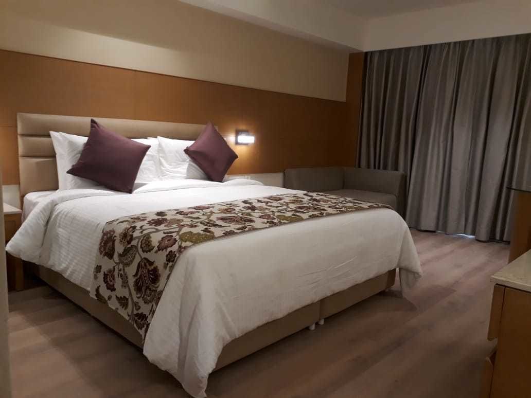 Una habitación de hotel con una cama grande, cabecera, mesita de noche y cortina.