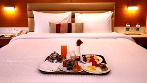 A neatly made bed with a tray of breakfast items including eggs, toast, and fruit, and a vase with a rose. - Nataraj Sarovar Portico Jhansi (Jhansi)