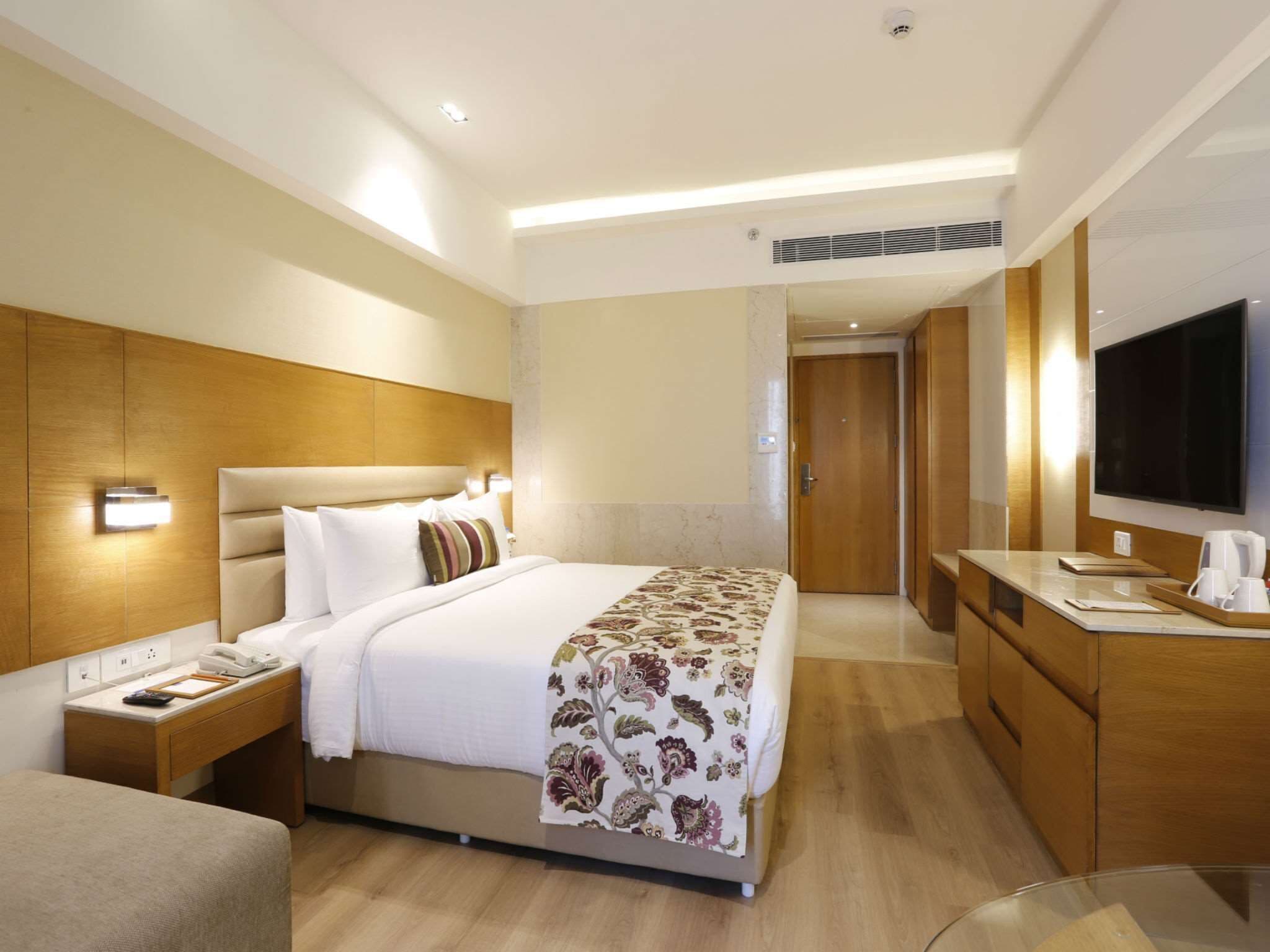 A hotel room with a bed, bedside table, lamp, and a TV on a stand.