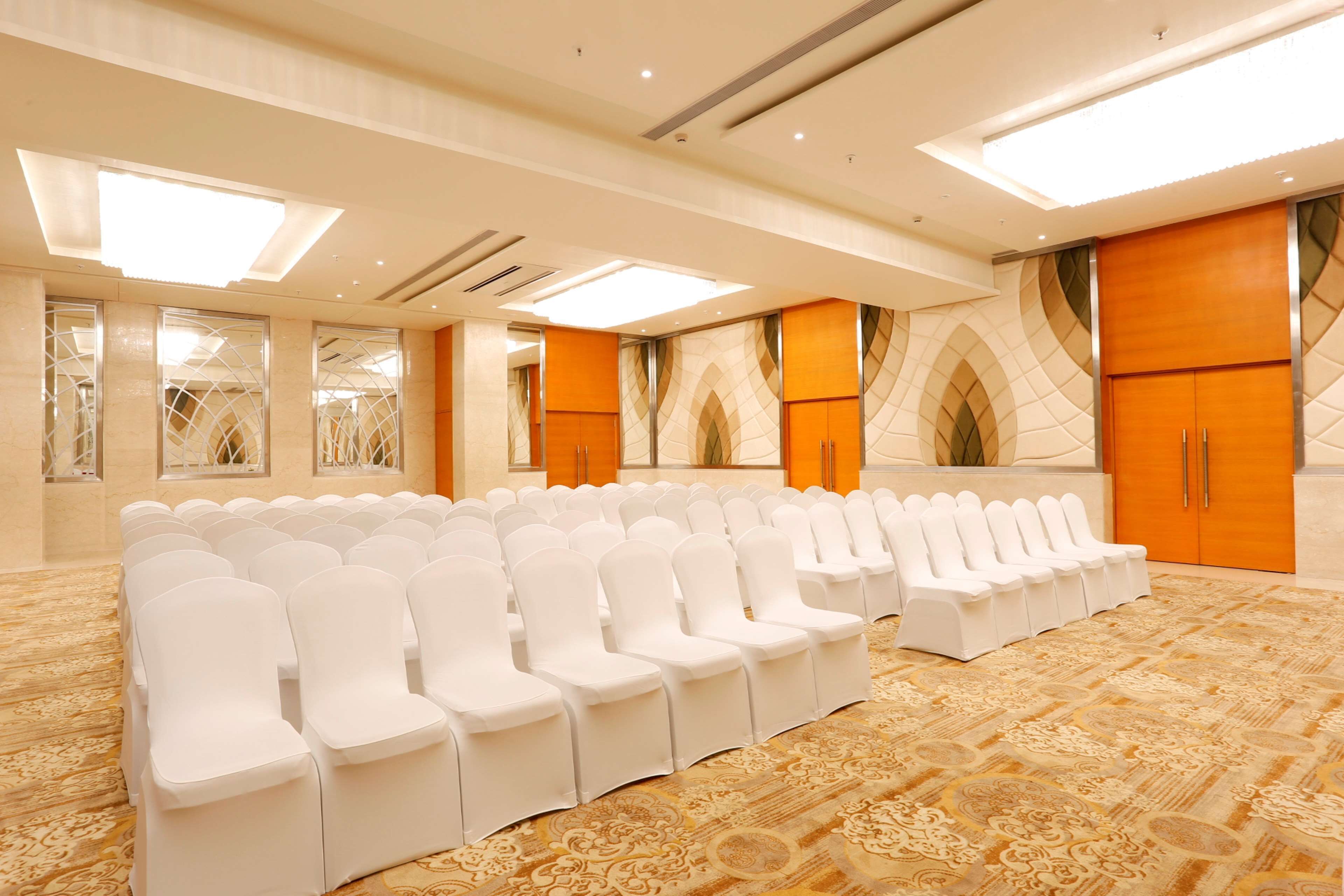 A conference room with rows of white chairs, a patterned carpet, and large wooden doors.