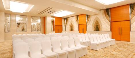 A conference room with rows of white chairs, a patterned carpet, and large wooden doors.