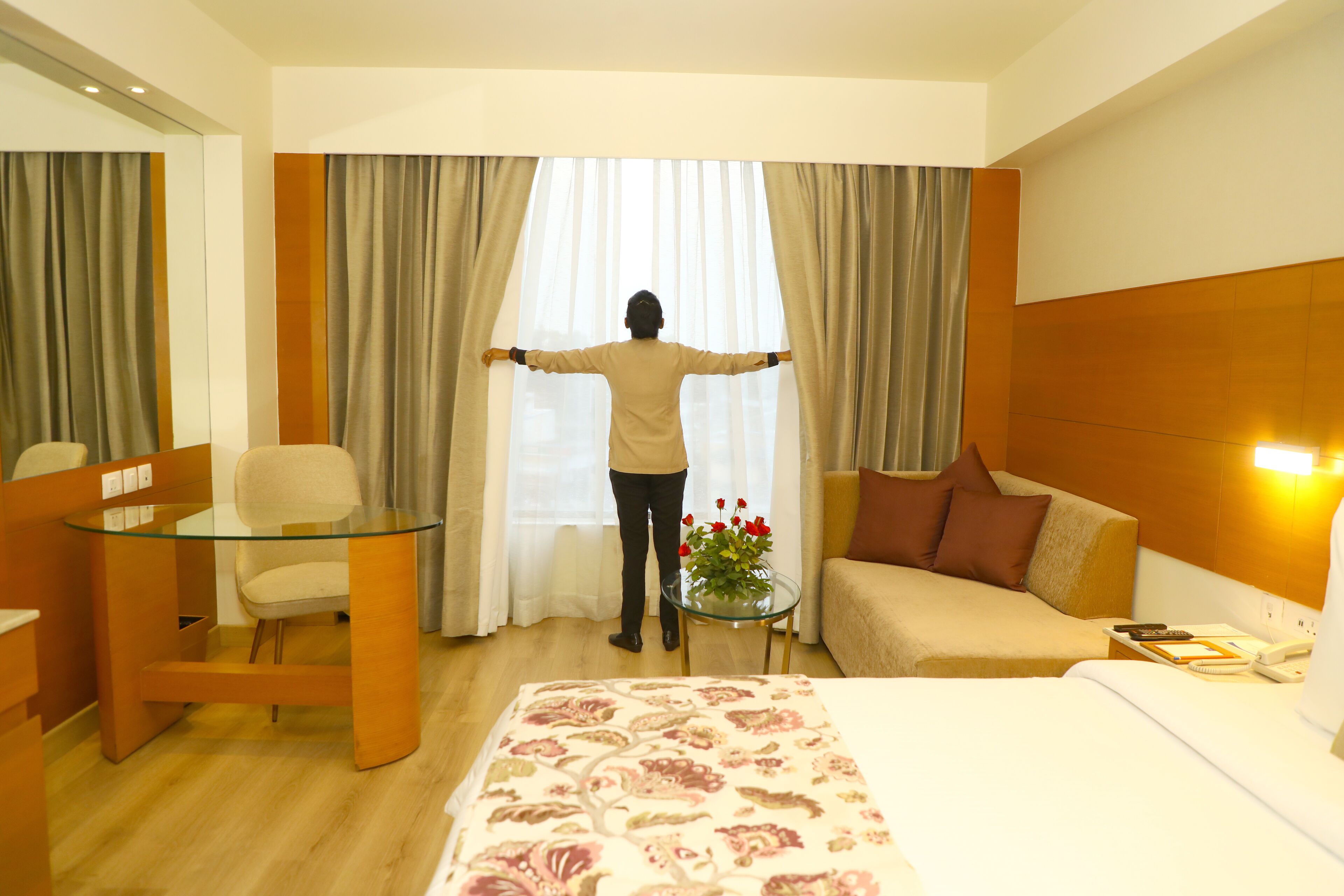 Ein Hotelzimmer mit einem Bett, einer Couch, einem Glastisch, einem Sessel und einem Fenster mit Vorhängen.