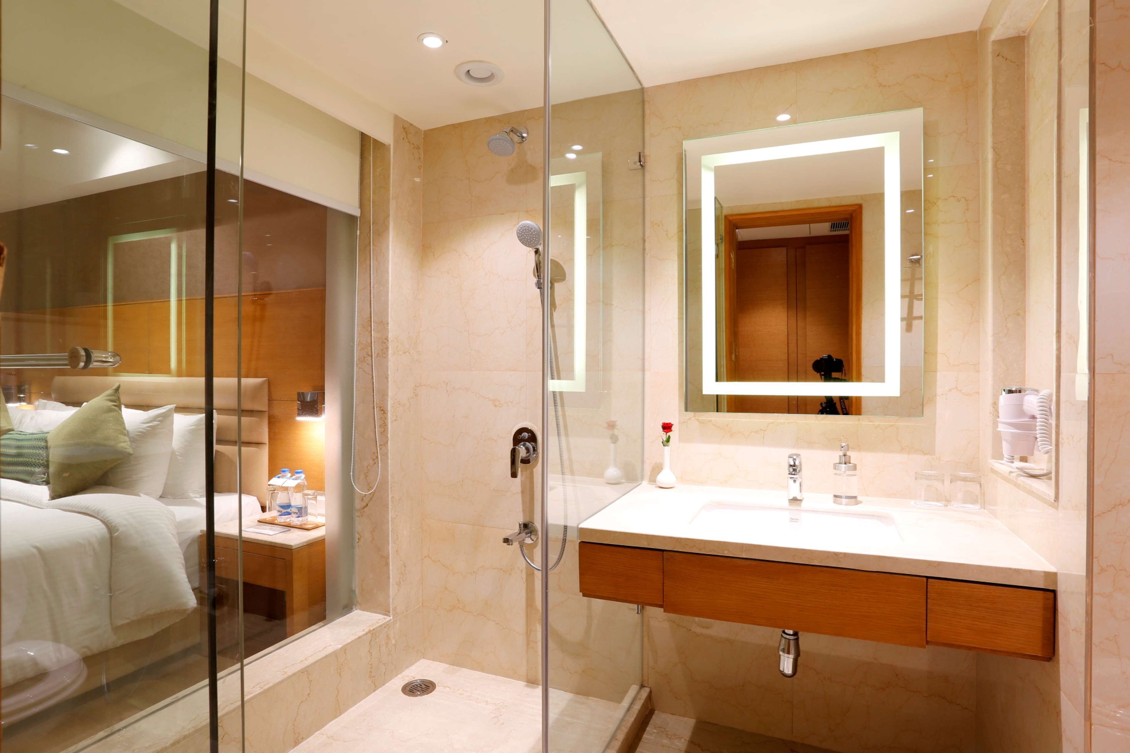 A modern hotel bathroom with a glass-enclosed shower, a large mirror, a white sink, and a wooden vanity.