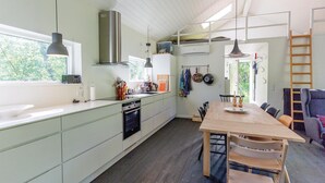 A modern kitchen with a large island, a dining area with a wooden table, and a view of the outdoors. - 3 bedroom awesome home in Højby (Højby)