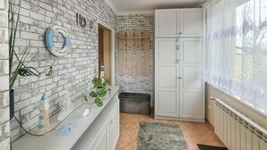 A room with a brick wall, a white wardrobe, a small bench, and a window with lace curtains.