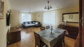 A dining area with a table set for four, a sofa, and a television on the wall.