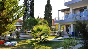 A courtyard with a palm tree, a red inflatable pool, and a multi-story building with balconies. - Alexanika Apartments (Sithonia)