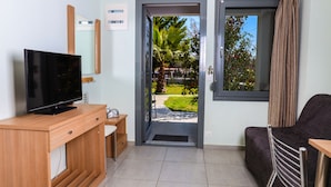 A modern room with a television on a wooden desk, a sofa, and a door leading to a garden. - Alexanika Apartments (Sithonia)