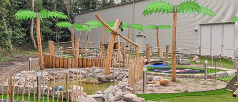 En zoologisk haveindhegning med et vandbassin, trækonstruktioner og en stor bygning i baggrunden.