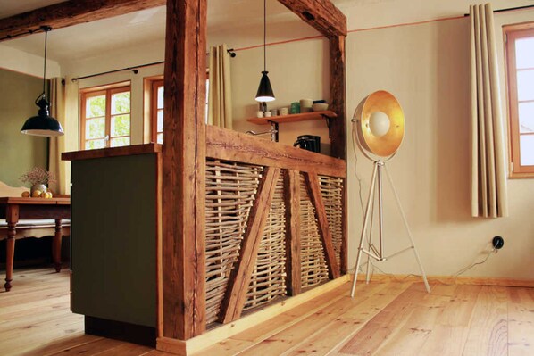 A room with wooden beams, a green cabinet, a wicker partition, a floor lamp, and a window with curtains.