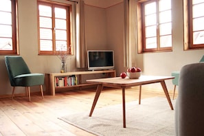A living room with a television, a wooden table, a green chair, and a bookshelf.