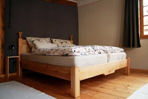 Een houten bed met een bedspread met dessin, in een kamer met houten vloeren en een donkere wand.