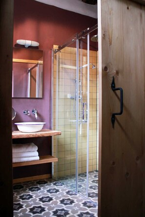 Een badkamer met een glazen douchecabine, een wit wastafelmeubel met paarse rand en een houten deur met een zwarte handgreep.