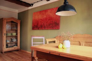 Een eetgedeelte met een houten tafel, stoelen, een kast met servies en een rode abstracte schildering aan de muur.