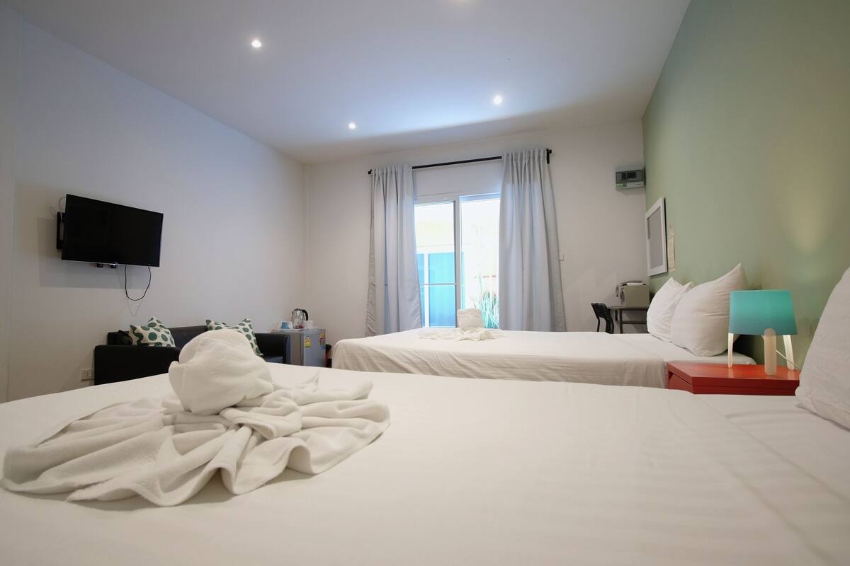 A hotel room with two beds, a flat-screen TV mounted on the wall, a desk with a chair, and a window with curtains.