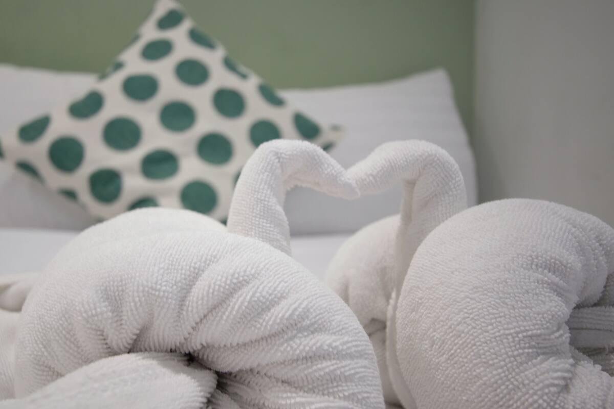 A bed with white bedding and a green polka dot pillow.