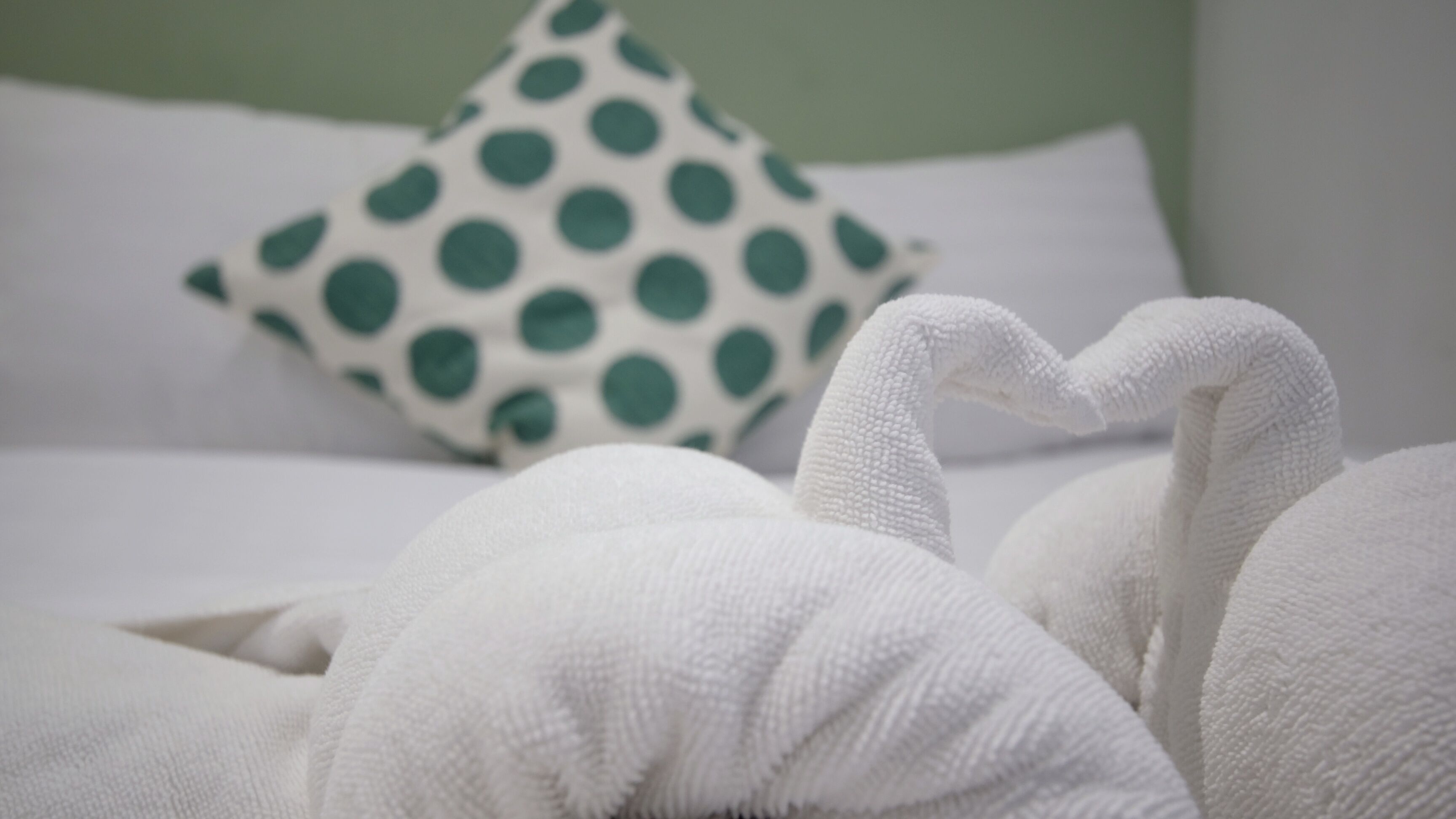 A bed with white bedding and a green polka dot pillow.