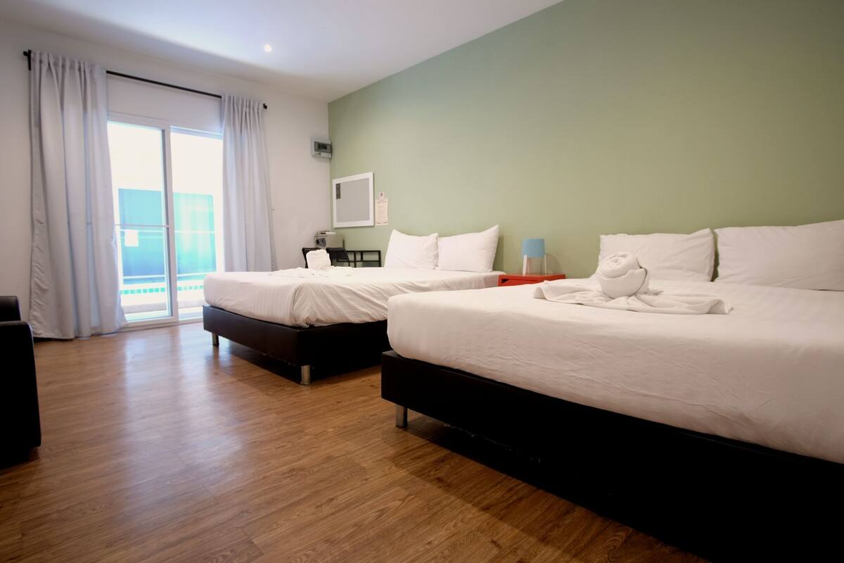 A hotel room with two beds, a desk, a chair, and a view of the outdoors.