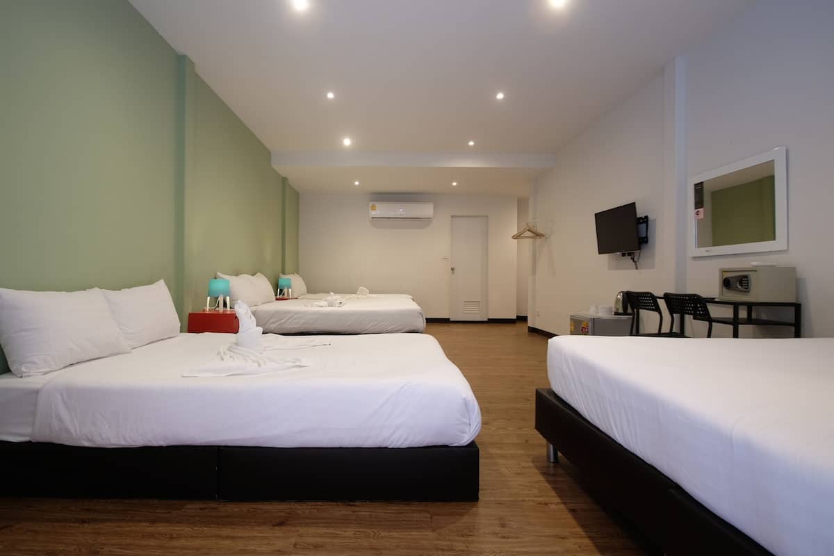 A hotel room with two beds, a TV, a desk with a chair, and an air conditioning unit.