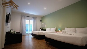 Une chambre d’hôtel avec deux lits, un plancher en bois, une télévision, une fenêtre avec des rideaux et une vue sur la mer.