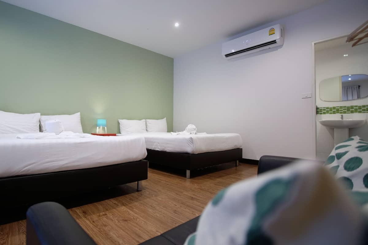 A hotel room with two beds, a desk, a chair, an air conditioning unit, and a bathroom with a sink and mirror.