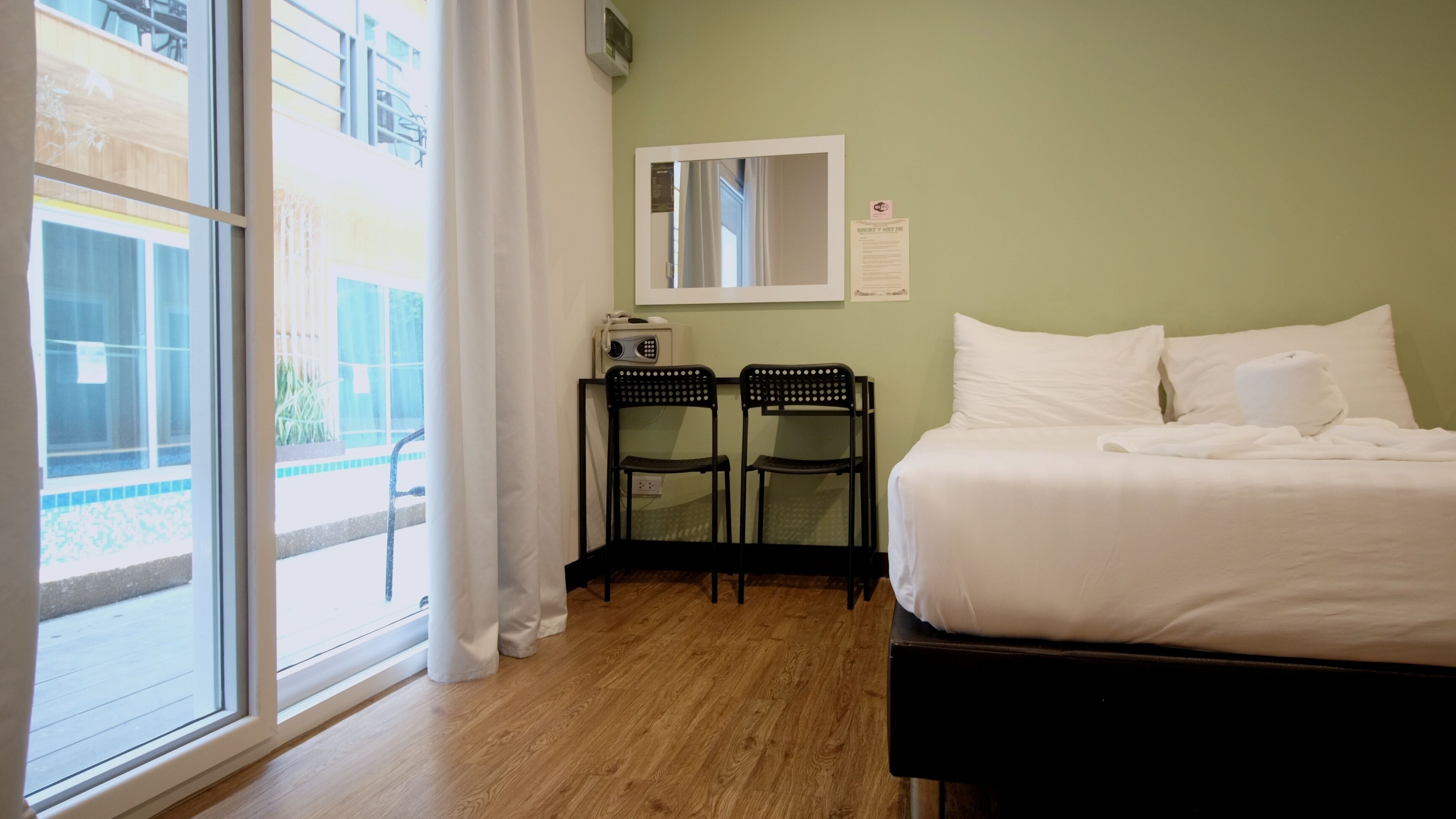 A hotel room with a large window, a bed, two chairs, a small table with a radio, and a mirror on the wall.